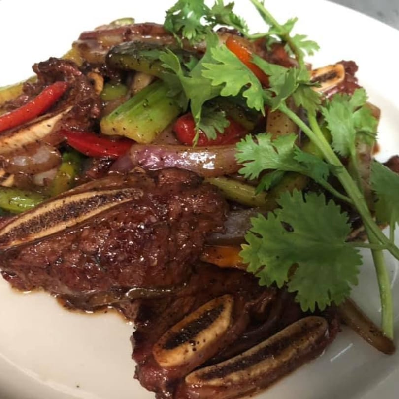 Grilled short ribs with red and green peppers, onions, and cilantro on a white plate.