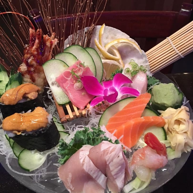 A vibrant platter of sushi and sashimi, including salmon, tuna, uni, and shrimp, garnished with a pink orchid.