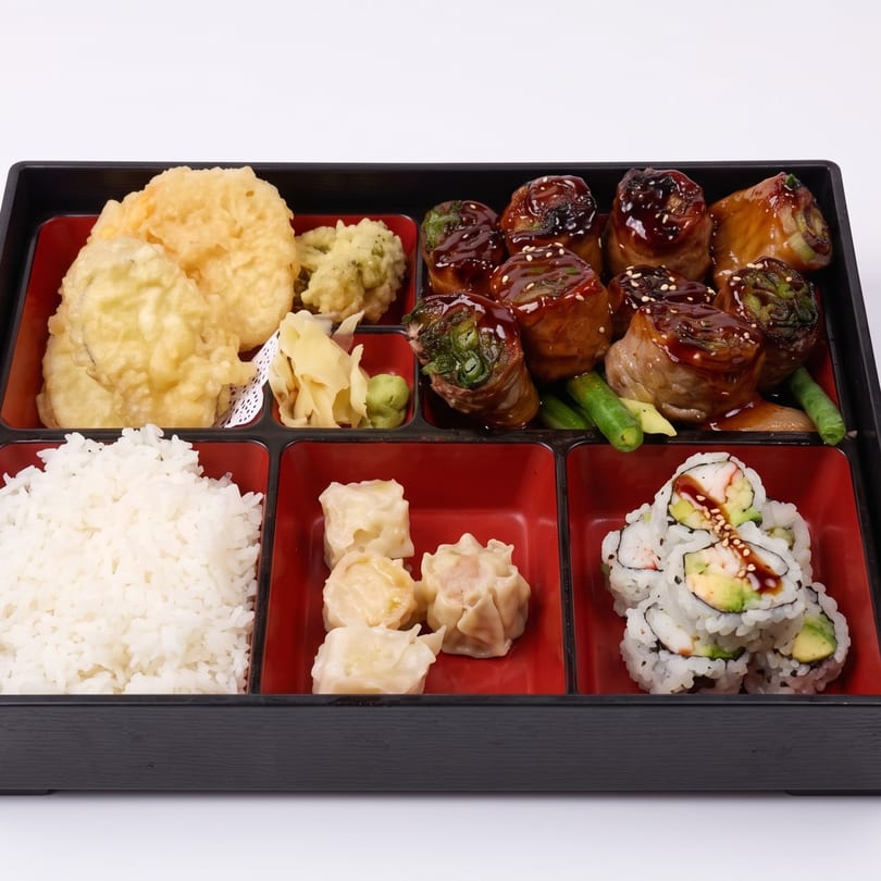 A bento box with tempura, beef rolls, rice, dumplings, and sushi rolls.